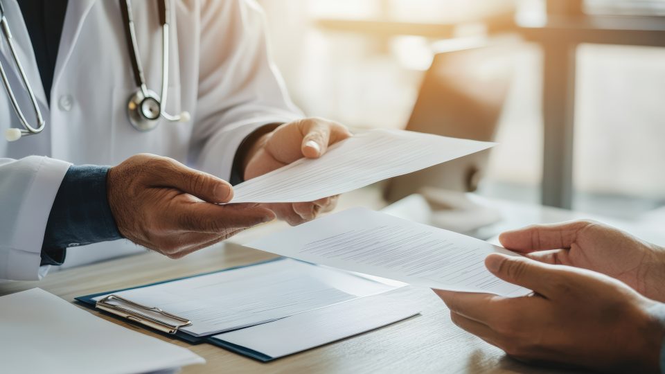 Doctor handing health insurance claim form to patient in bright modern clinic office demonstrating healthcare administration billing process and medical insurance coverage discussion